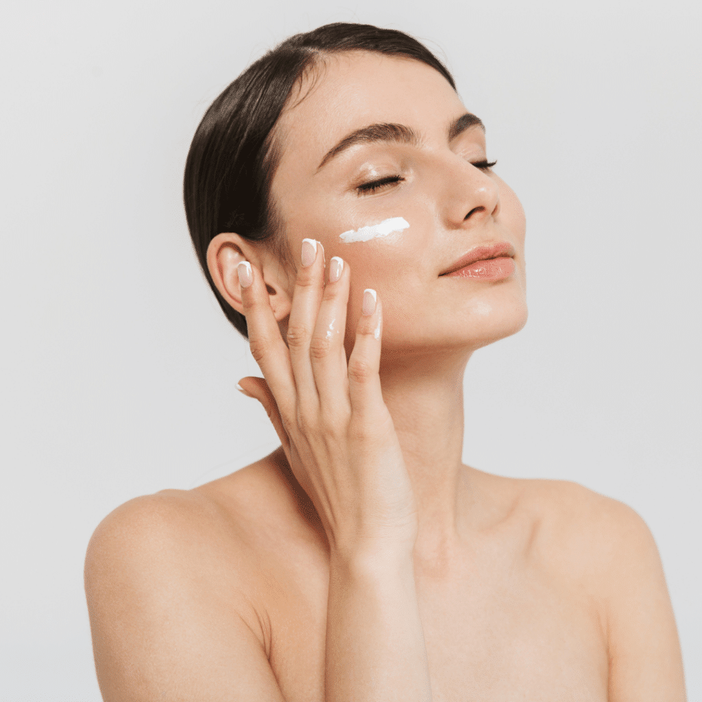 In & Out Skincare - Femme heureuse qui se met de la crème sur la joue